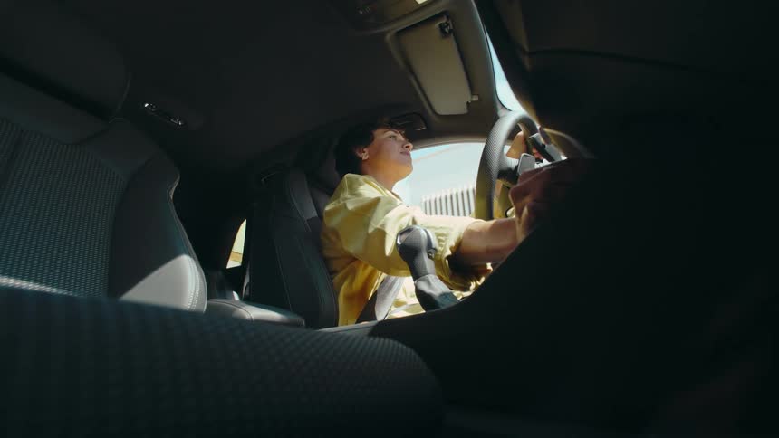 Side POV from the car floorboard of a woman driving and turning the radio volume up on the control panel.