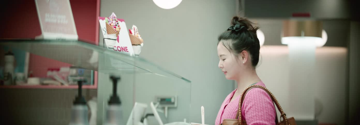 Woman in pink sweater smiles while choosing toppings at a frozen yogurt shop
