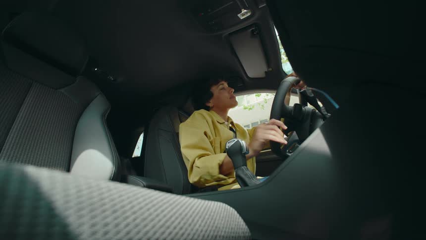 POV from the passenger floorboard of a woman driving a car as she looks back and happily engages with someone in the backseat and then looks forward again while swaying and singing to music.