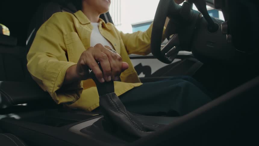 Low angle view looking up from the floorboards of a happy woman with her hand on the steering wheel putting an automatic vehicle into gear.