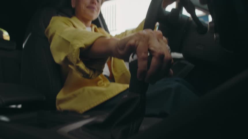 Low angle view from the floorboard looking upward of a woman in the driver's seat of a car as she engages the gear shift stick in a vehicle
