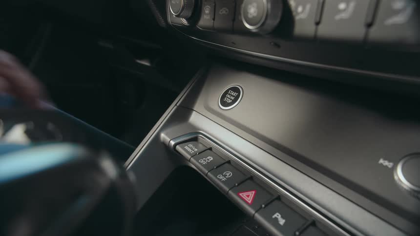 Close up of a person's finger pressing the engine start button inside a parked car.