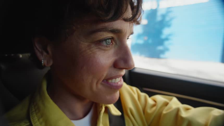 Close up of the face of a middle-aged woman with short hair, bright blue eyes, and a big smile in the driver's seat of a vehicle preparing to drive off.