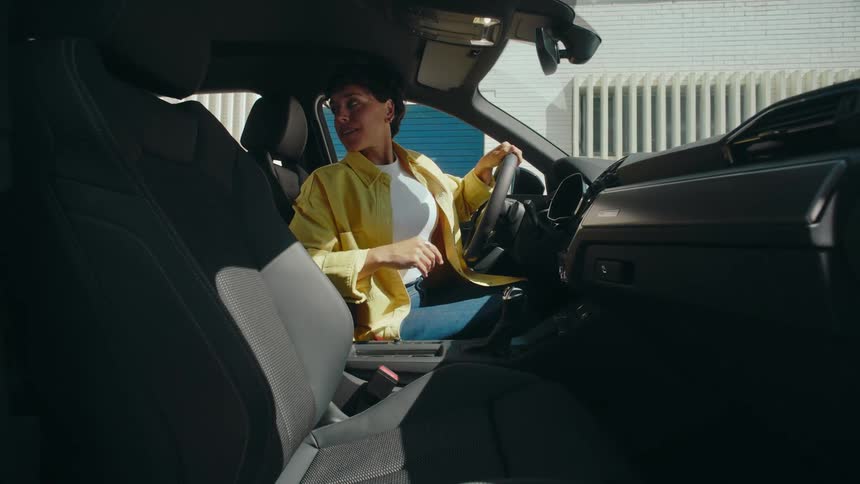 A woman gets in the driver's side seat of her SUV and puts her seatbelt on, then adjusts her rearview mirror.