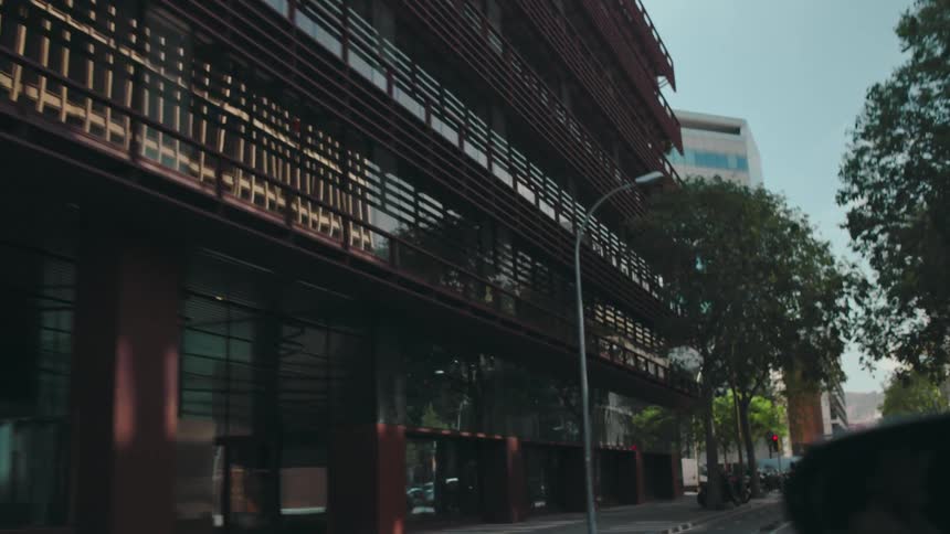 POV from the side of a car as it is driven through a modern city street lined with trees and glass buildings