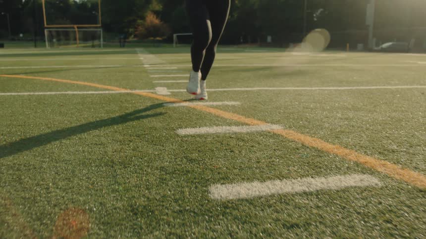 Female jogger runs down a football field on a summer day