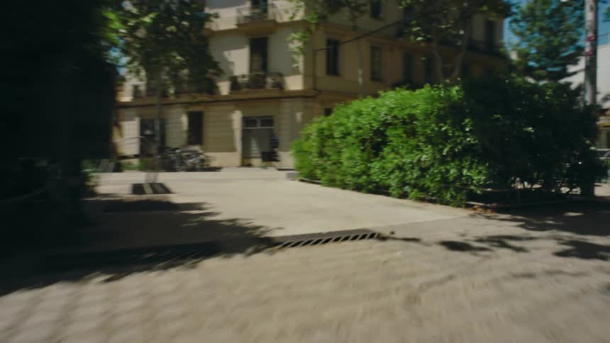 Low angle tracking shot through a paved green area in the city with an apartment building and parked bicycles.