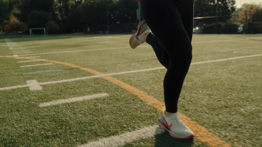 A woman is running on the football field on a sunny day