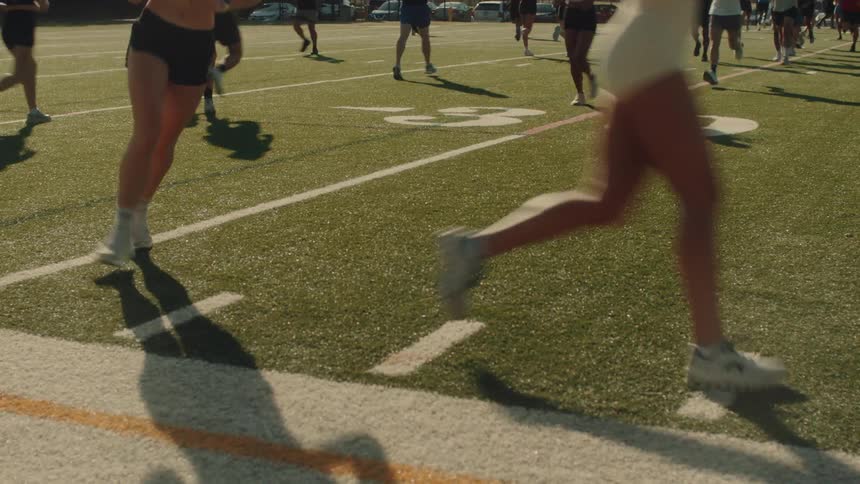 Legs of several people running on a sports grass field