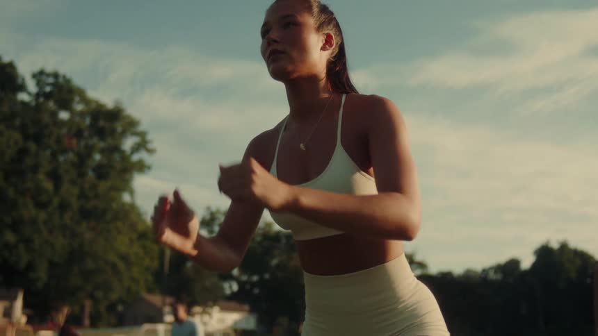A young woman exercises with a group of adults on a field during the day