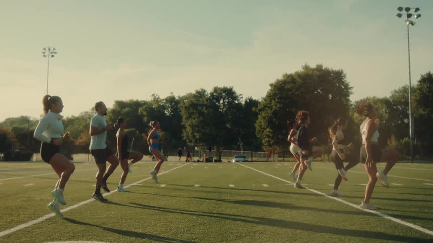 A group of people perform highknee exercises together on a sunny outdoor athletic field
