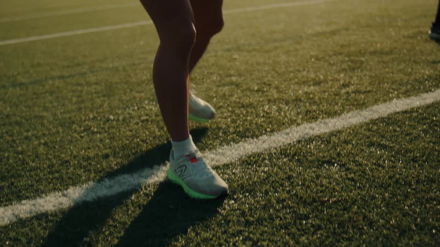 A female athlete is tying her shoelace on a sunlit sports field