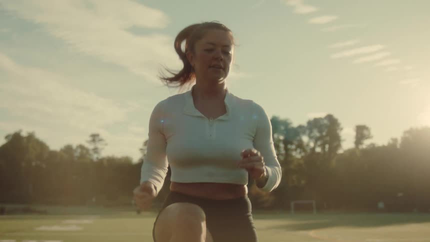 An athlete in a longsleeved shirt and shorts is performing high knees as a warmup on a sports field