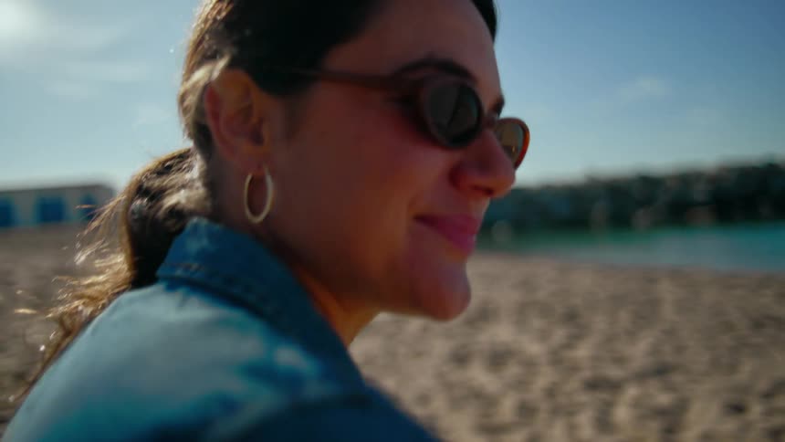 A woman talking to another person sitting on the beach sand with a dog beside them on a sunny day