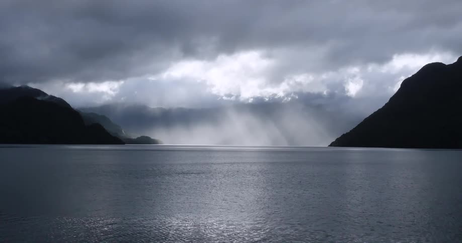 Light rays pierce through dark clouds over a still harbor
