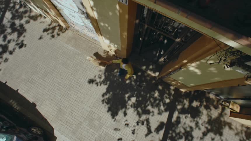 Woman walking her dog exits a building and is pulled to the right by the leash as the animal rushes excitedly down the sidewalk.