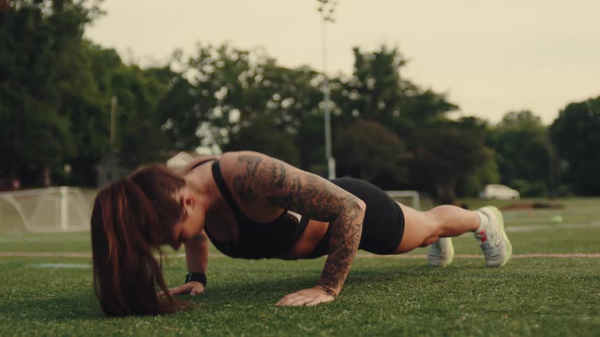 Woman does push ups on the turf of the football field on a summer day
