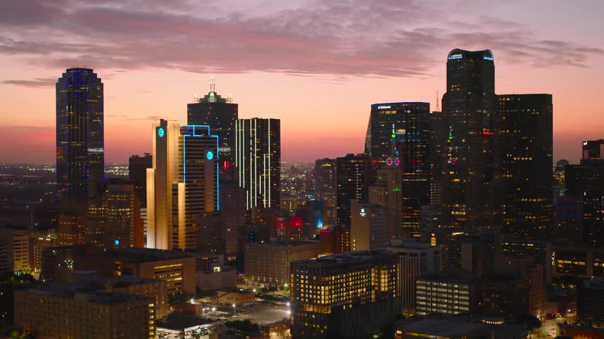 A vibrant city skyline is captured at dusk with skyscrapers lit up against a colorful evening sky
