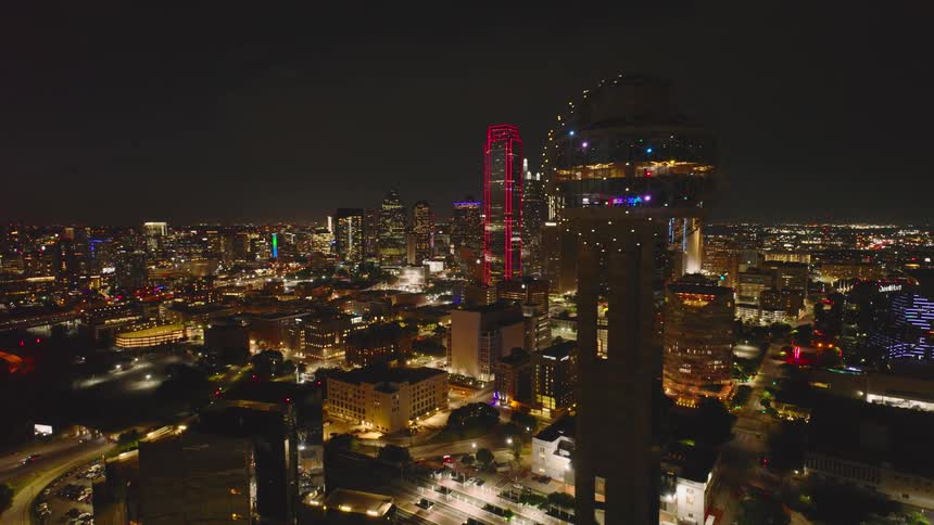 Aerial night view of a brightly lit city skyline featuring illuminated skyscrapers and bustling streets