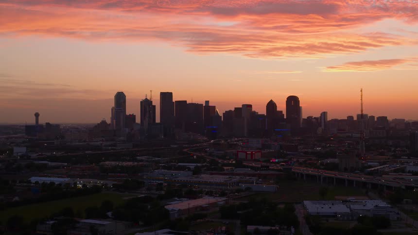 A wide aerial shot captures the dallas city skyline at sunset with glowing orange clouds overhead