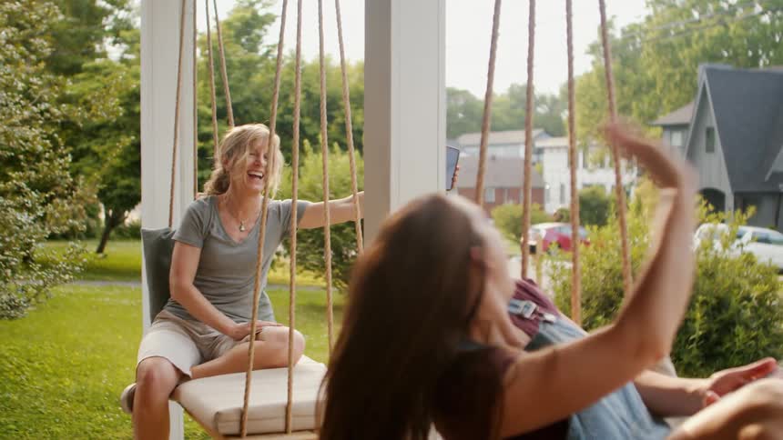 A mother and daughter sit outside on porch swings together
