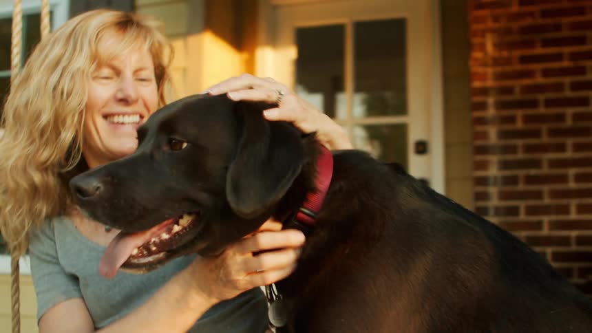 A woman is petting the dog on the porch