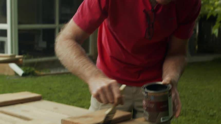Man with a brush applying varnish to a piece of wood