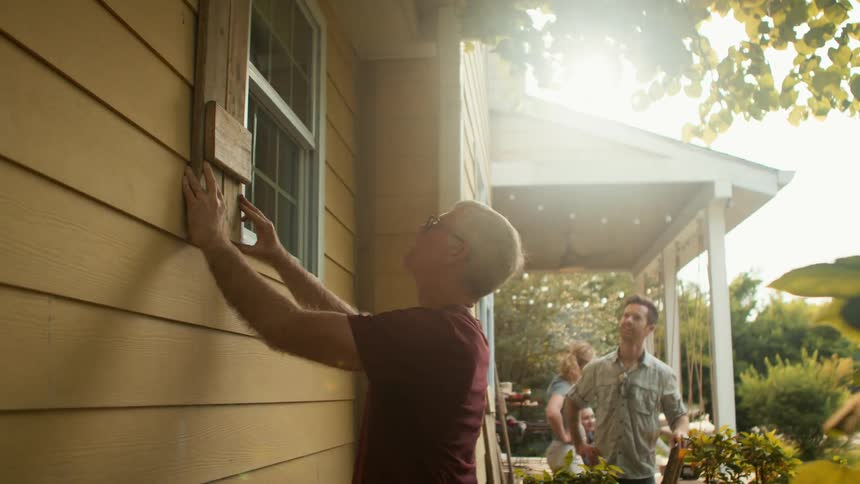 Man placing a wooden slat on a window from the outside