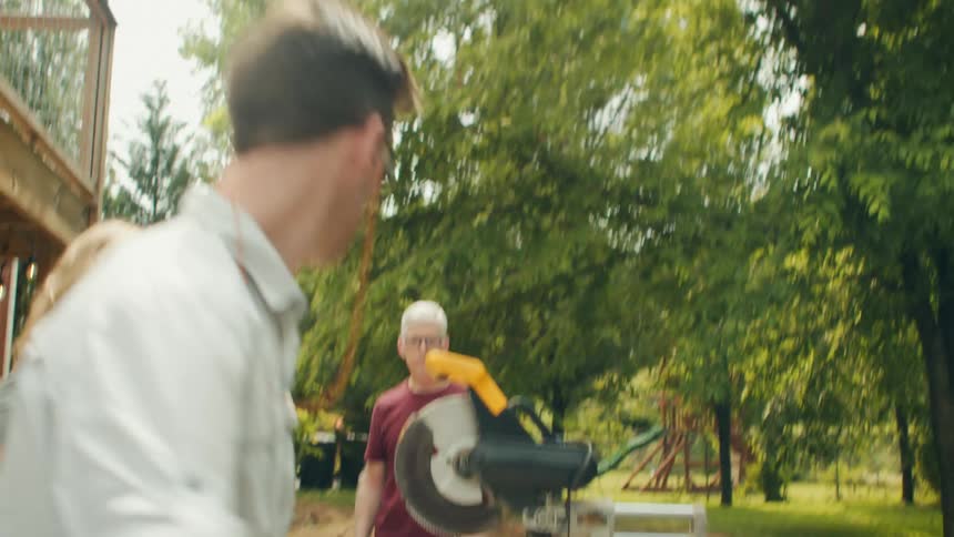 Man picking up a wooden slat and placing it towards a circular saw in the backyard of a house