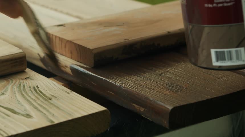 Hand with brush applying varnish to a wooden slat