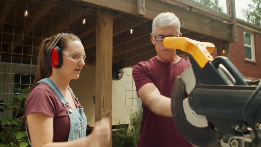 Family wearing protective gear handling a circular saw in the backyard of a house