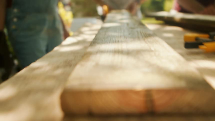 Close up of a wooden plank placed on an outdoor worktop by a man