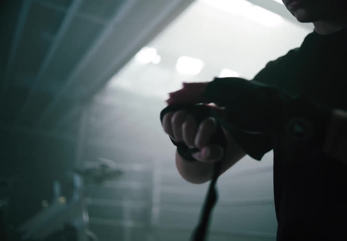 A woman wraps her hands with boxing tape in preparation for training inside a dimly lit gym