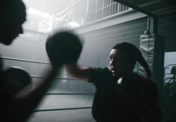 Two boxers train together in a dimly lit gym outside the ring