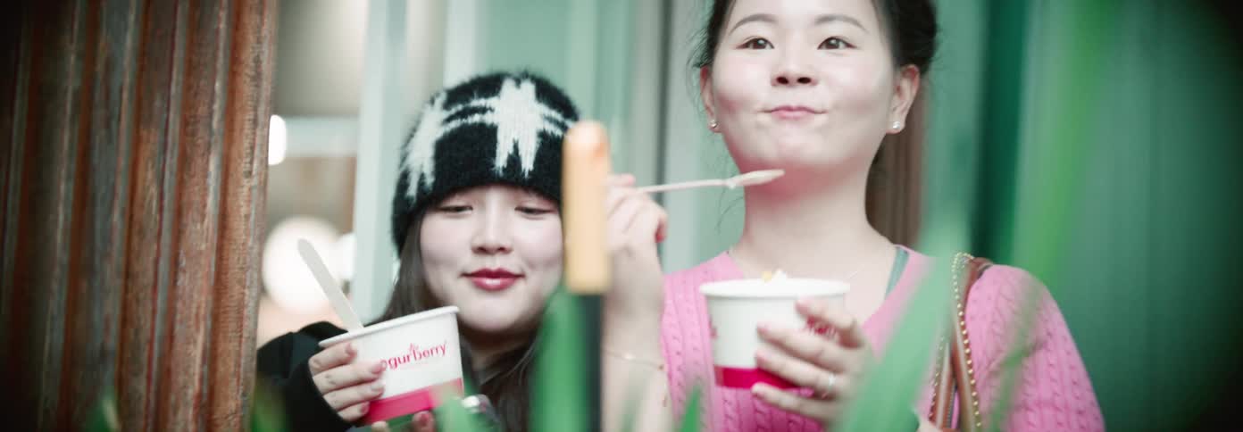 Two women happily enjoy frozen yogurt while chatting outdoors