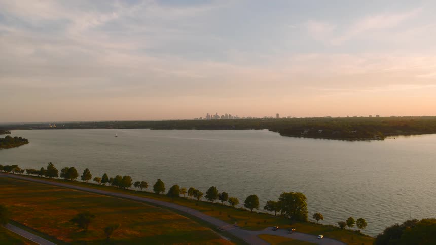Aerial view of a lake at sunset with a treelined road and distant city skyline