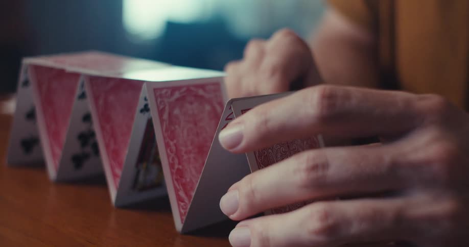 A person carefully builds a house of cards on a wooden table