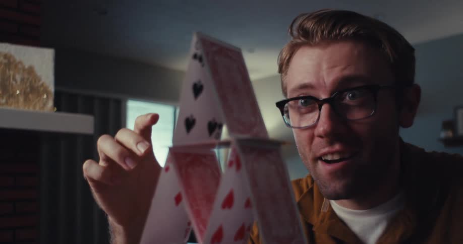 A man happily builds a pyramid with playing cards at home