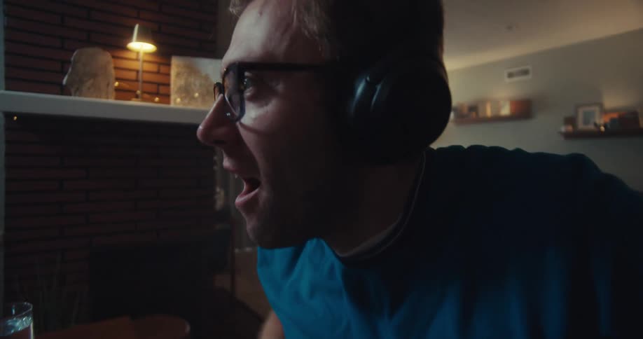 A man wearing a headset excitedly celebrates a win in front of a computer screen