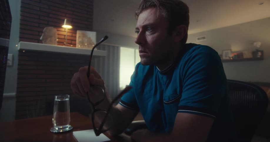 A man sitting at a desk looking at a computer monitor puts his glasses on and starts to type