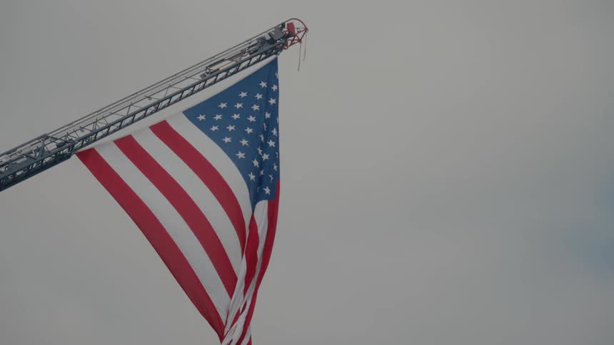 An american flag that hangs from a crane high in the air is blowing in the wind