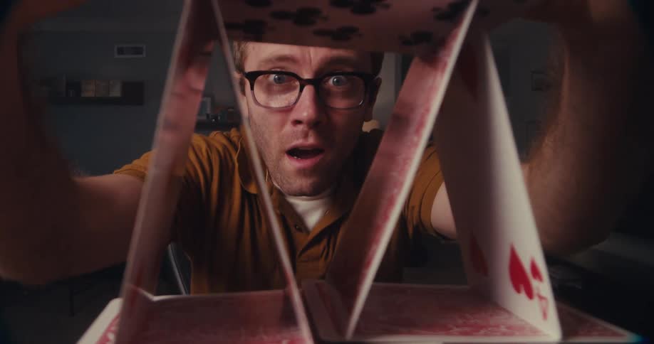 A man puts the finishing playing cards in a triangle on top of a card tower and celebrates by putting his fists in the air