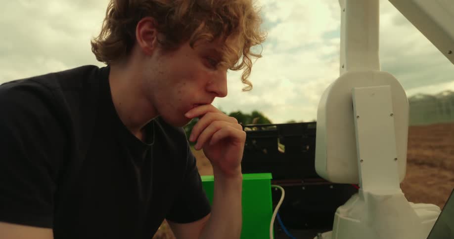 A man is using his laptop to repair a agricultural robot