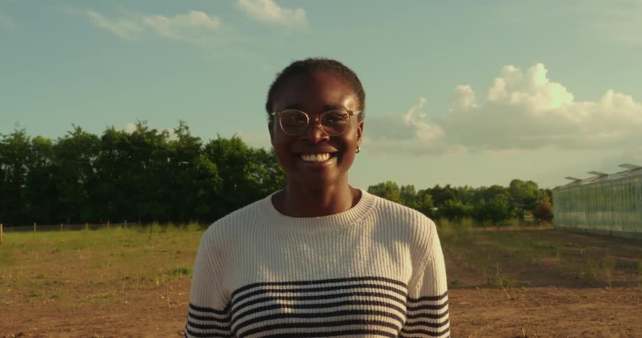 Black woman stands and smiles in the middle of a field during the day