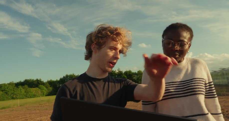 A man walks with a woman on the farm while holding a laptop