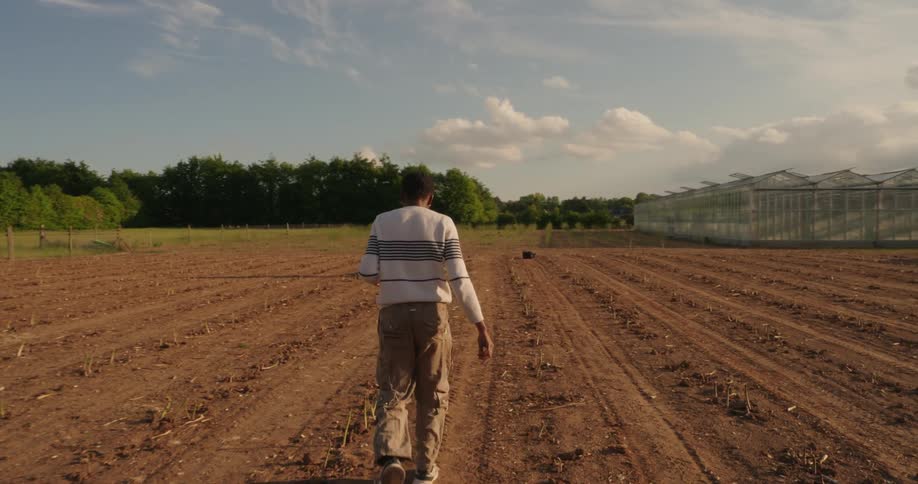 A man walks through a tilled field toward another man near robotic farm equipment