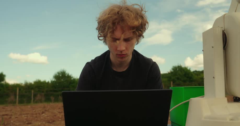 The man is using a laptop to work on an agricultural robot