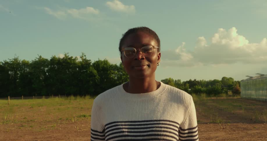 A young black woman wearing glasses standing in an agricultural field on a sunny day