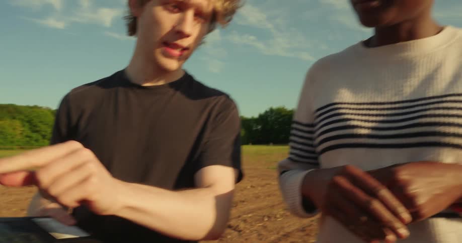 Two people stand in an agricultural field discussing about work while holding a laptop