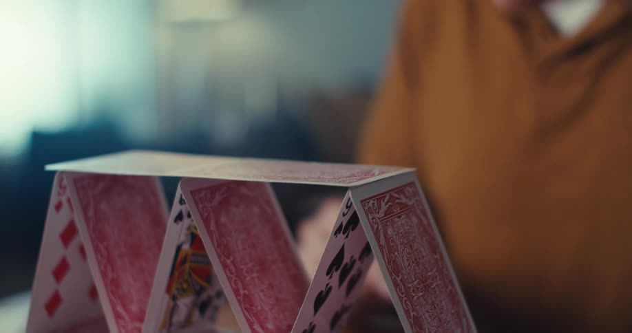 A man carefully stacks playing cards to build a card pyramid in a closeup shot